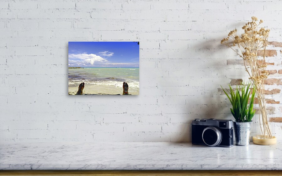 A scene of a counter top with a photo on the wall of a person feet looking out to a ocean scene.